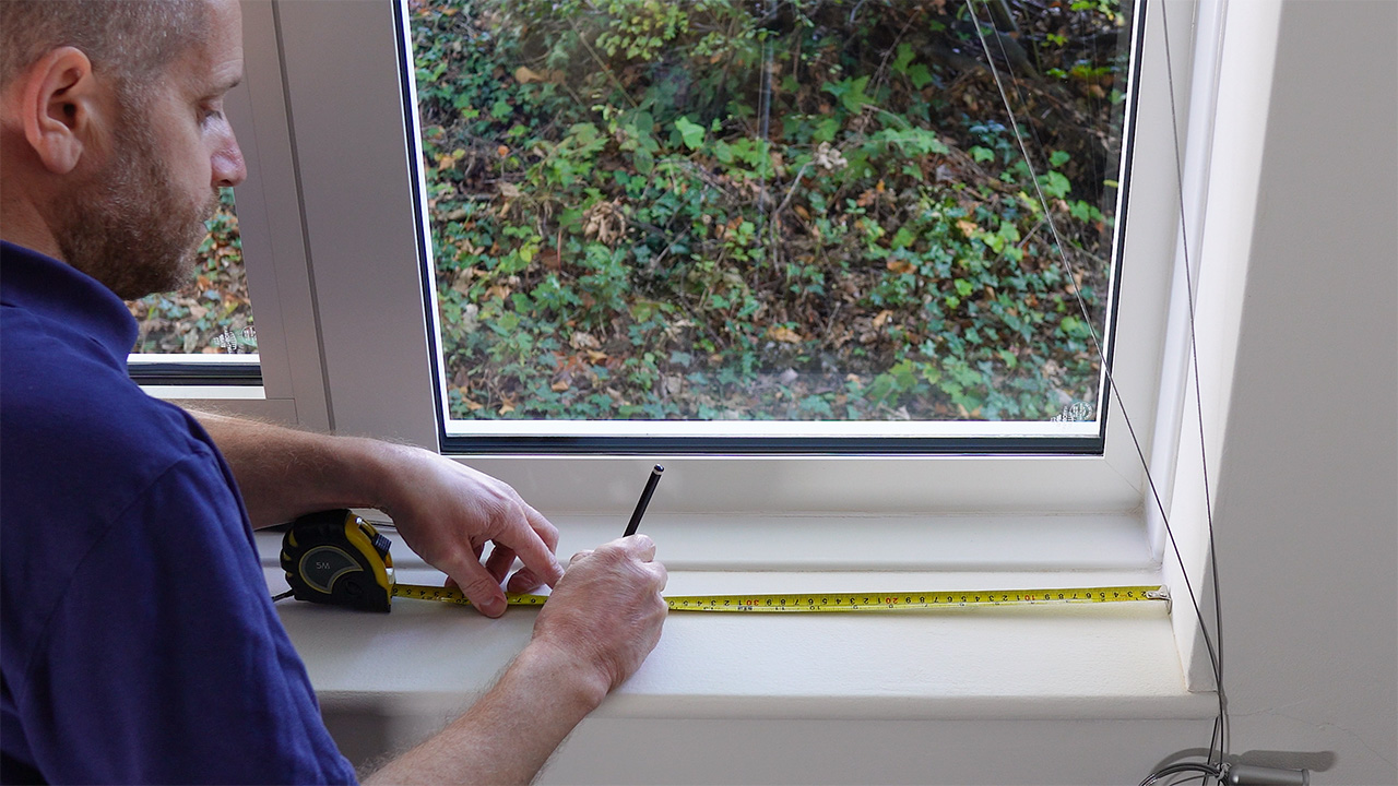 Tape measuring the hole centres for the bottom fixings of a cable-suspended poster display kit.