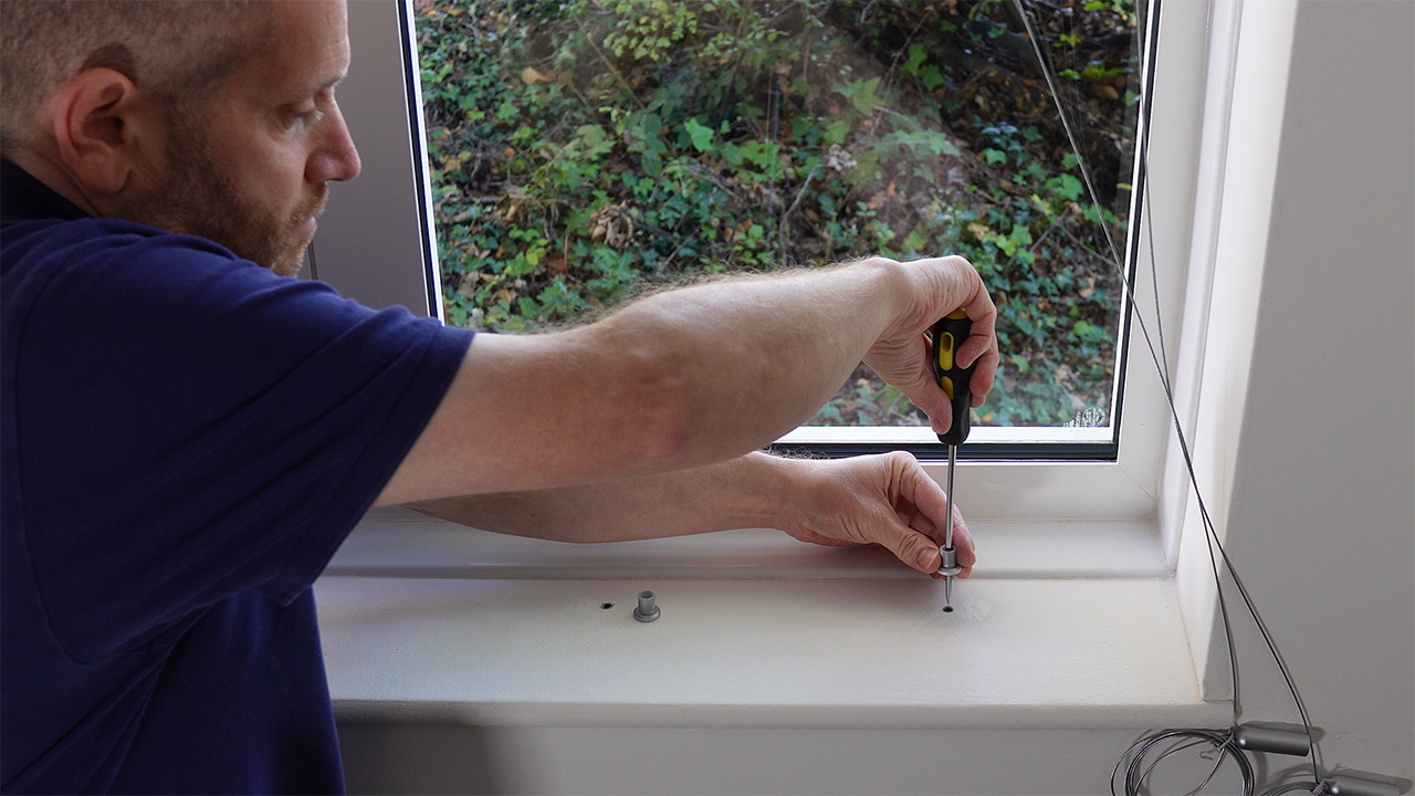 Attaching the cable kit's bottom inner fixing to the window recess.