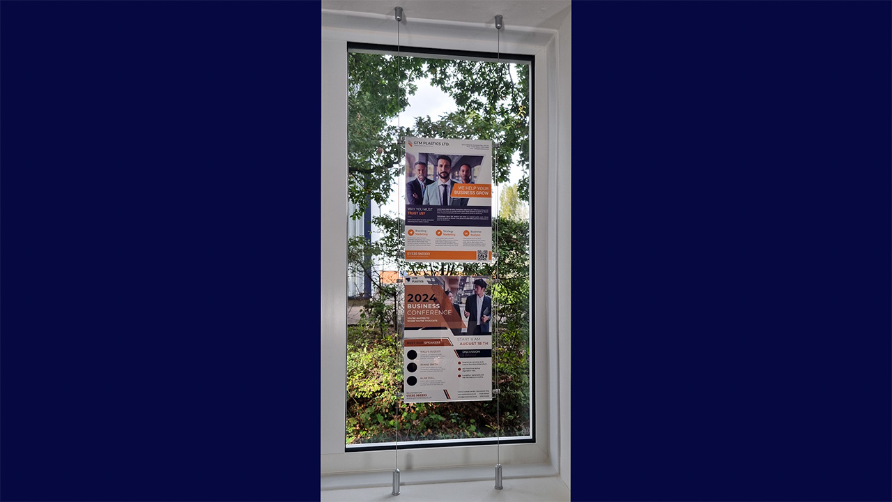 A fully assembled cable suspended poster display attached from floor to ceiling, being used as a window display.