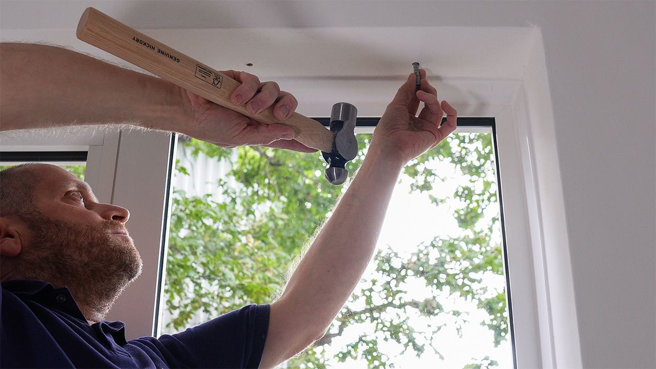 Gently hammering a plastic fixing plug into a drilled hole.