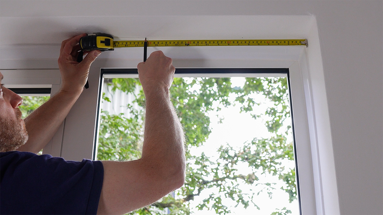 Tape measuring the hole centres for the top fixings of a cable-suspended poster pocket display kit.