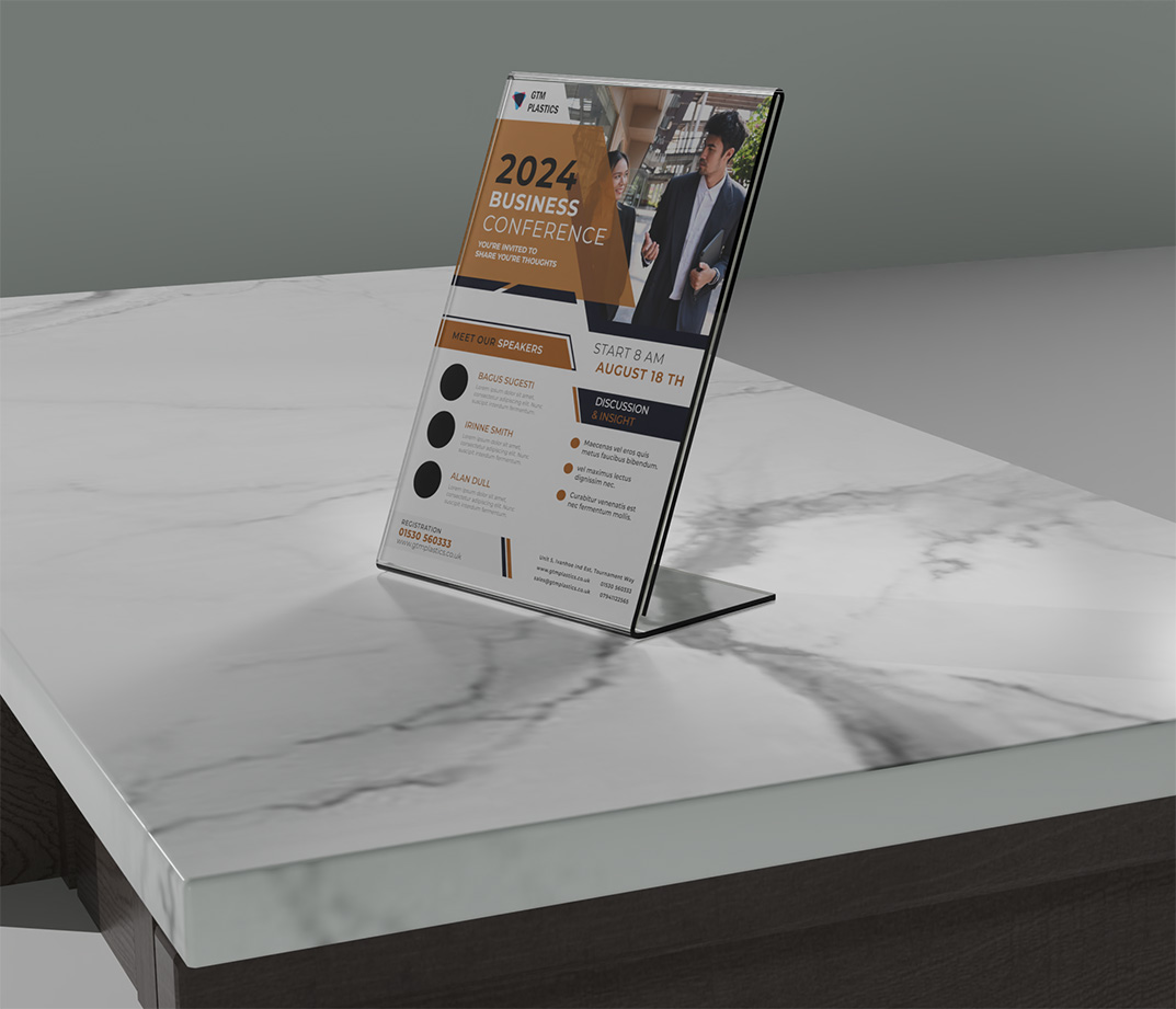 A sloping acrylic poster holder sitting on a marble top counter. The poster is advertising a business conference.