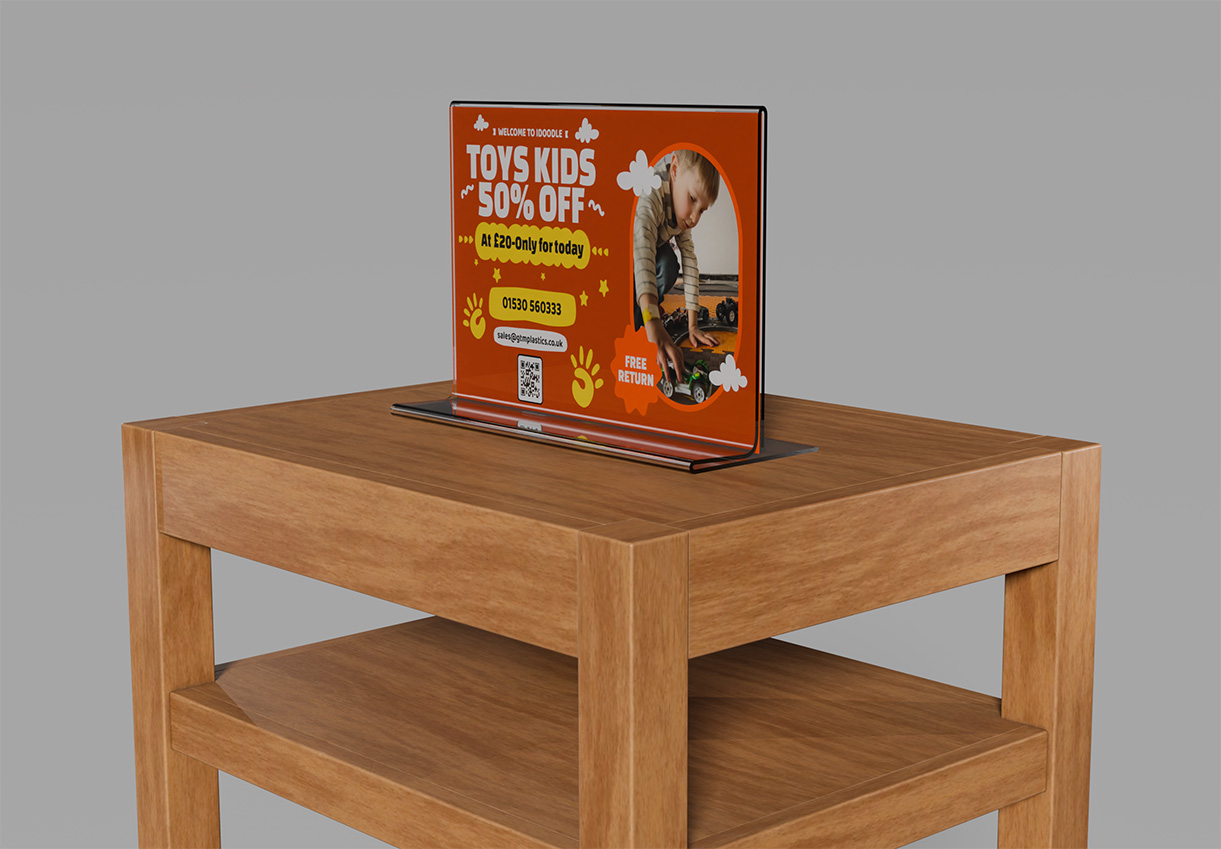 A free-standing upright acrylic poster holder placed on a small two-level wooden table. The poster is advertising 50 percent off all kids toys.