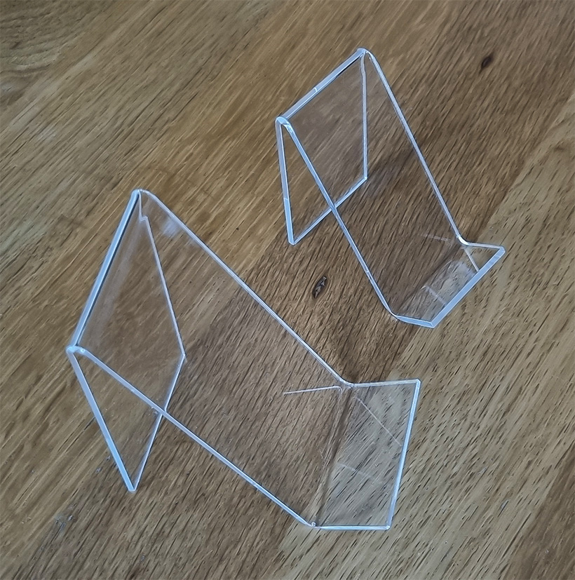 Two different size mobile phone stands manufactured from clear acrylic, placed on a desk side by side.